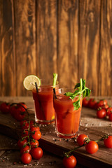 selective focus of bloody mary cocktail in glasses on wooden background with salt, pepper, tomatoes and celery
