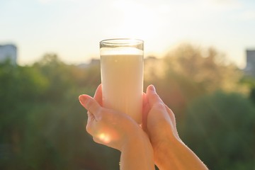 Glass with milk in womans hand, background sunset