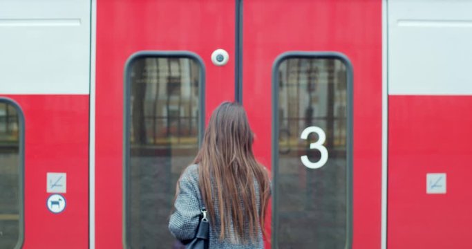 Back view of woman catching the train on railway platform slow motion handheld device. Brunette girl traveler stepping inside wagon going on vacation. Commuting transportation urban lifestyle
