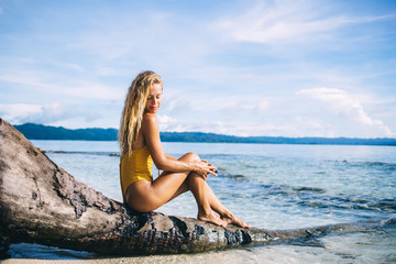 Fototapeta na wymiar Young blonde sitting on dead tree on beach