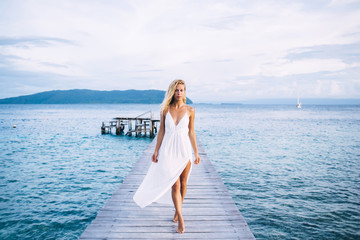 Alluring slim female in light dress standing on boardwalk