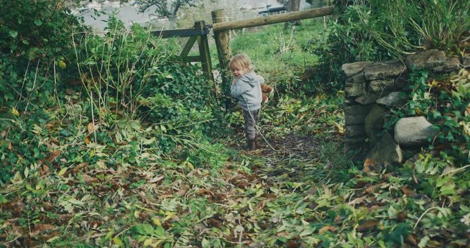 Little toddler with teddybear walking to gate in the woods