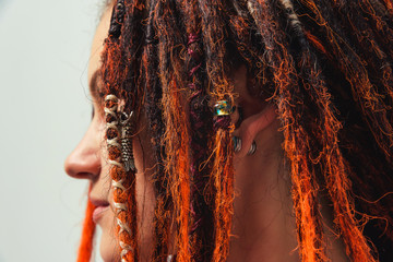 Girl with red fire dreadlocks on white background side view. A young woman with long dreadlocks on...