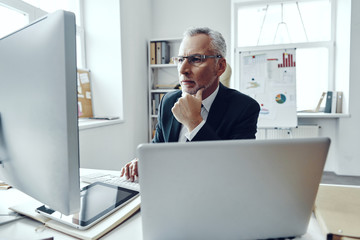 Senior man in elegant business suit using modern technologies while working in modern office