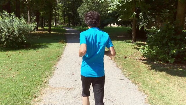 young sportsman in a blue T-shirt runs on the path of the park of the royal villa of Monza while the camera follows him