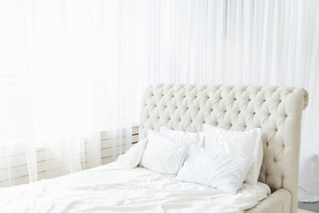 White bedroom with light bed and high headboard, light from the window