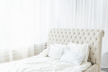 White bedroom with light bed and high headboard, light from the window