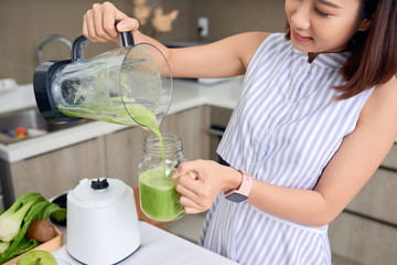 Beautiful Asian woman pouring smoothie from blender in the kitchen
