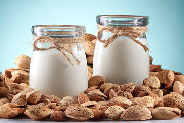 Almond milk in bottles among almonds, blue background