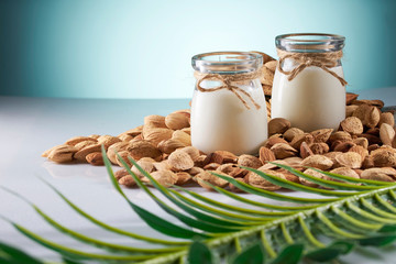 Almond milk in bottles among almonds, blue background
