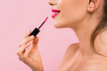 cropped view of smiling naked beautiful woman with pink lips applying lip gloss isolated on pink