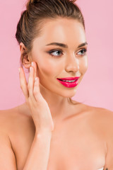 smiling naked beautiful woman with pink lips posing with hand near face and looking away isolated on pink