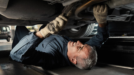 Mechatroniker repariert Auto in Werkstatt von unten