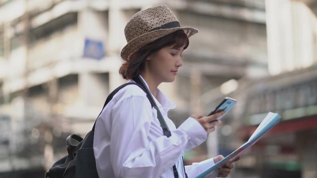 Beautiful woman tourist using online maps on the smartphone and paper maps in the city street