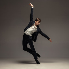 Man in casual office style clothes jumping and dancing isolated on grey background. Art, motion,...