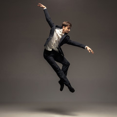 Man in casual office style clothes jumping and dancing isolated on grey background. Art, motion, action, flexibility, inspiration concept. Flexible caucasian ballet dancer, weightless jumps.