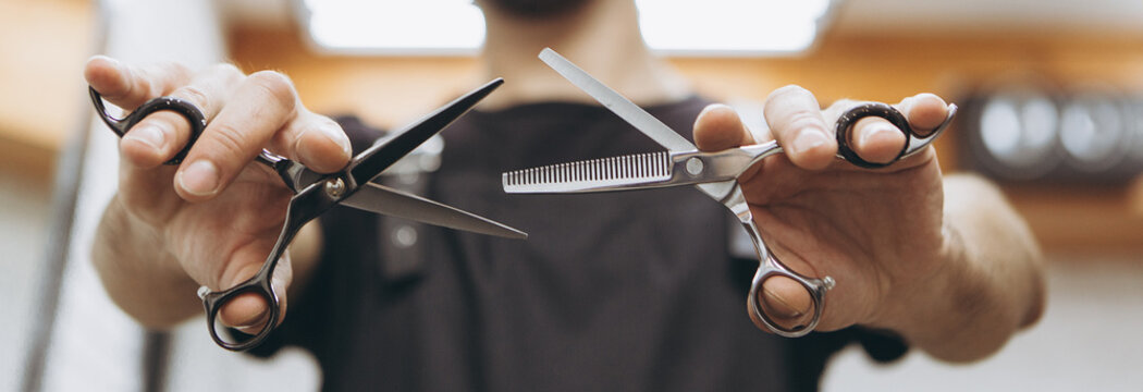 Professional hairdresser prepares for a haircut, checks his tool, examines scissors holding them in his hands, focus on scissors. concept for barbershops, beauty salons and hairdressers