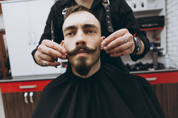 stylish attractive man with a beard in a barbershop. Shaving and modeling a contemporary beard shape in retro style, the barber shaves his client