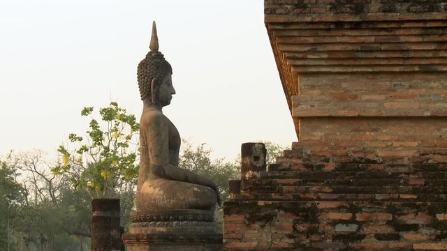 Wide side view of a seated Buddha image facing a brick wall of a temple at Sukhothai Historic Park