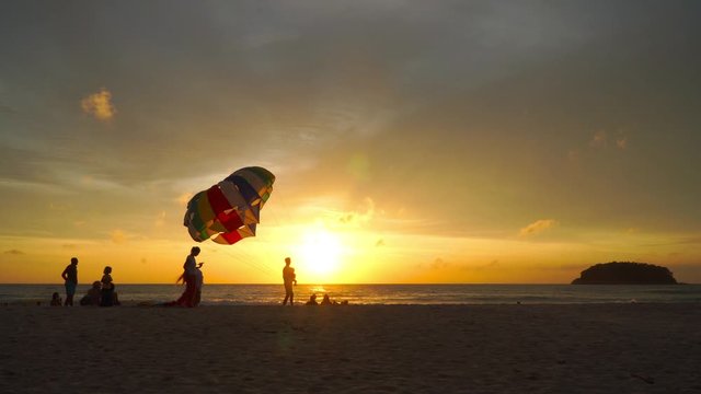 Phuket,Thailand-October,19,2019:mother and father carry a child to take a photo with parasailing  background in golden sunset at Kata beach Phuket Thailand