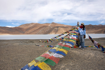 Travelers thai woman travel visit stand for take photo with Prayer flag for blessing at viewpoint with mountains and Pangong lake while winter season at Leh Ladakh in Jammu and Kashmir, India