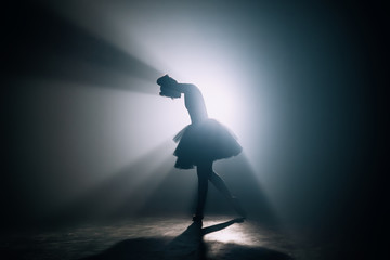 Silhouette of ballerina who has finished dancing her part in performance on stage. Distressed woman bowed her head. Stress, problems concept. - obrazy, fototapety, plakaty