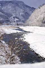 Fototapeta na wymiar 春の魚野川、雪ぼうしをかぶった小石が点々