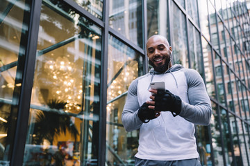 Cheerful black guy with earphones browsing smartphone