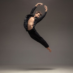Man in casual office style clothes jumping and dancing isolated on grey background. Art, motion, action, flexibility, inspiration concept. Flexible caucasian ballet dancer, weightless jumps.