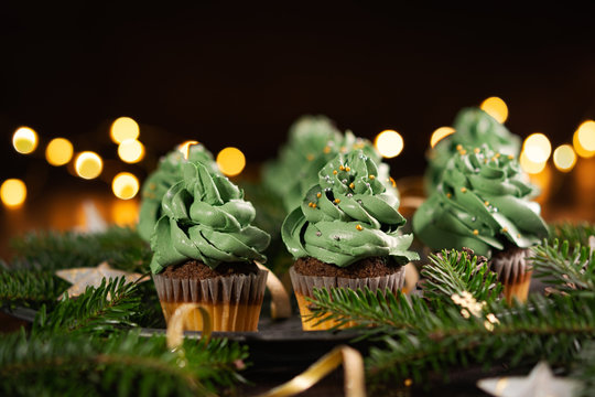 Banner Christmas tree cupcakes sweet dessert with golden sprinkles on wooden background with garland lights bokeh. Close up. Christmas and new year holidays background concept.