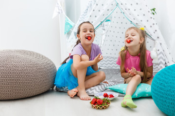 two little girls eat strawberries at home near wigwam tent © Angelov