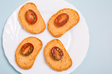 Tostadas con hummus y tomates cherry en un plato sobre fondo azul celeste.