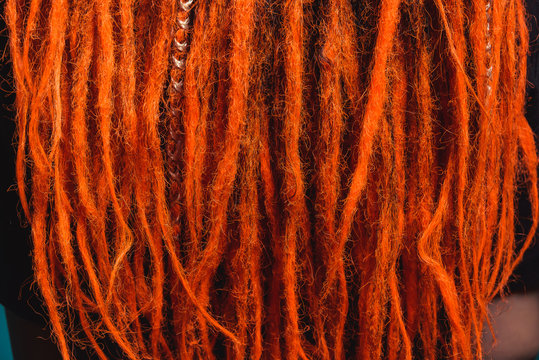 Dreadlocks orange red close-up. Braiding dreadlocks from natural hair. A girl with fiery red dreadlocks back view.