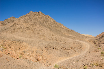 desert mountain landscape photography in clear weather day time with sand stone rocks and lonely dirt trail 