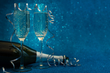 Two glasses of champagne and bottle decorated streamers on blue glittering background. Christmas and New Year holidays concept. Copy space. © thayra83