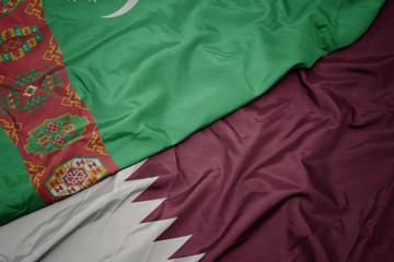 waving colorful flag of qatar and national flag of turkmenistan.