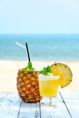 pineapple juice with sliced pineapple fruit on wooden table with abstract blue sea background , summer fruit drink concept