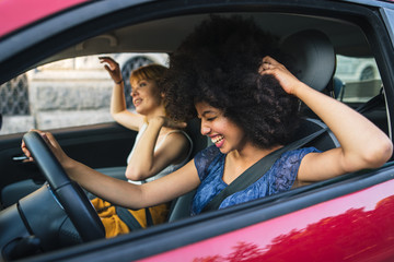 Two young women friends driving in the city - Millennials use the car to get around - obrazy, fototapety, plakaty
