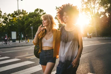 Fotobehang Paar jonge vrouwen die bij zonsondergang op straat lopen - Twee millennials omarmd in de stad © loreanto