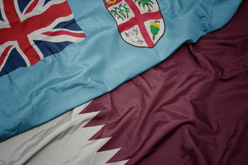 waving colorful flag of qatar and national flag of Fiji .