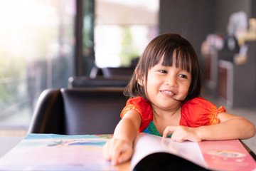 Adorable asian little girl is sitting and reading storybook on the sofa with concentrate happy moment, concept of activity for kid education.