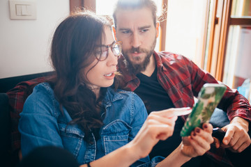 Young couple sitting couch indoor at home using smartphone