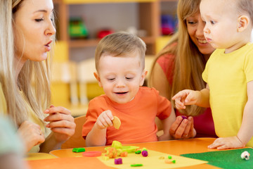 Little kids having fun together with moms. Creative kids molding at home. Children boys playing with plasticine or dough.