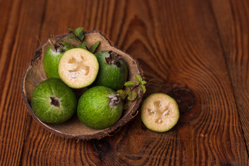 Green feijoa in a coconut shell hulf on a wooden background. Ripe tropical fruits, raw vegan food.Vitamin C. Copy space.