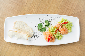 Salmon tartare with cucumber and sesame seeds. Tasting dish on a wooden table.