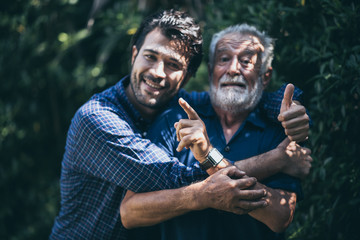 An adult hipster son and his senior father in garden, hugging