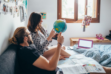 Young couple lying on bed planning travel looking at world map