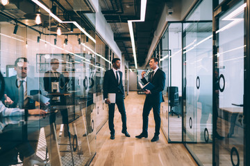 Businessman explaining opinion for ethnic colleague while standing in office corridor