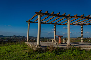 A place to relax on a hill overlooking the houses below. Table and chairs made of stone, roof, gazebo. Portugal