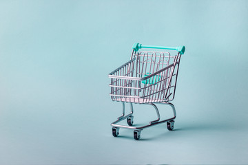 Small empty shopping cart on bright blue background with copy space